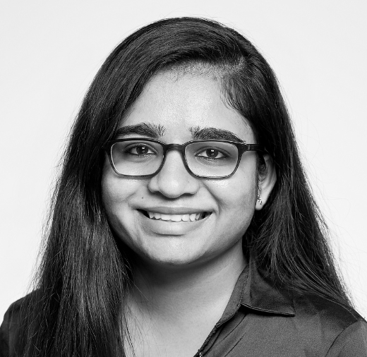 A person with long hair and glasses smiles in a black and white portrait.
