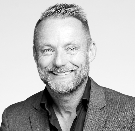 Black and white portrait of a smiling man with short hair and a beard, wearing a suit jacket and shirt.