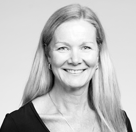 A woman with long hair smiles in a black and white portrait. She is wearing a V-neck top and a necklace.
