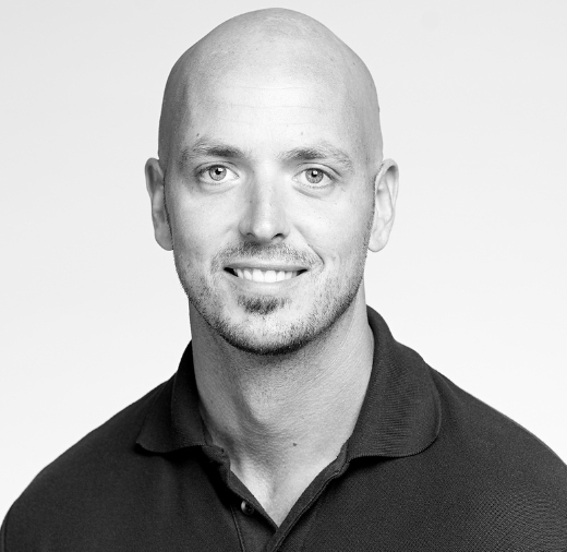 Black and white portrait of a bald man with a beard, wearing a collared shirt, and smiling at the camera.