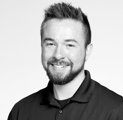 A black-and-white headshot of a smiling man with short hair and a beard, wearing a collared shirt.