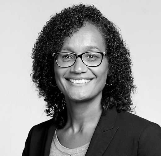 A person wearing glasses and a blazer, smiling against a plain background in a black-and-white photograph.
