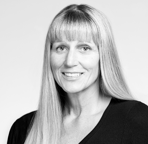 Black and white portrait of a smiling person with long straight hair and bangs, wearing a dark top.