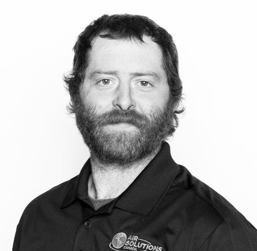 Man with a beard wearing a black Air Solutions Canada shirt, looking at the camera. Black and white image.
