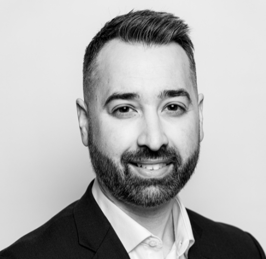 Black and white portrait of a man with short hair and a beard, wearing a suit jacket and shirt, smiling slightly.