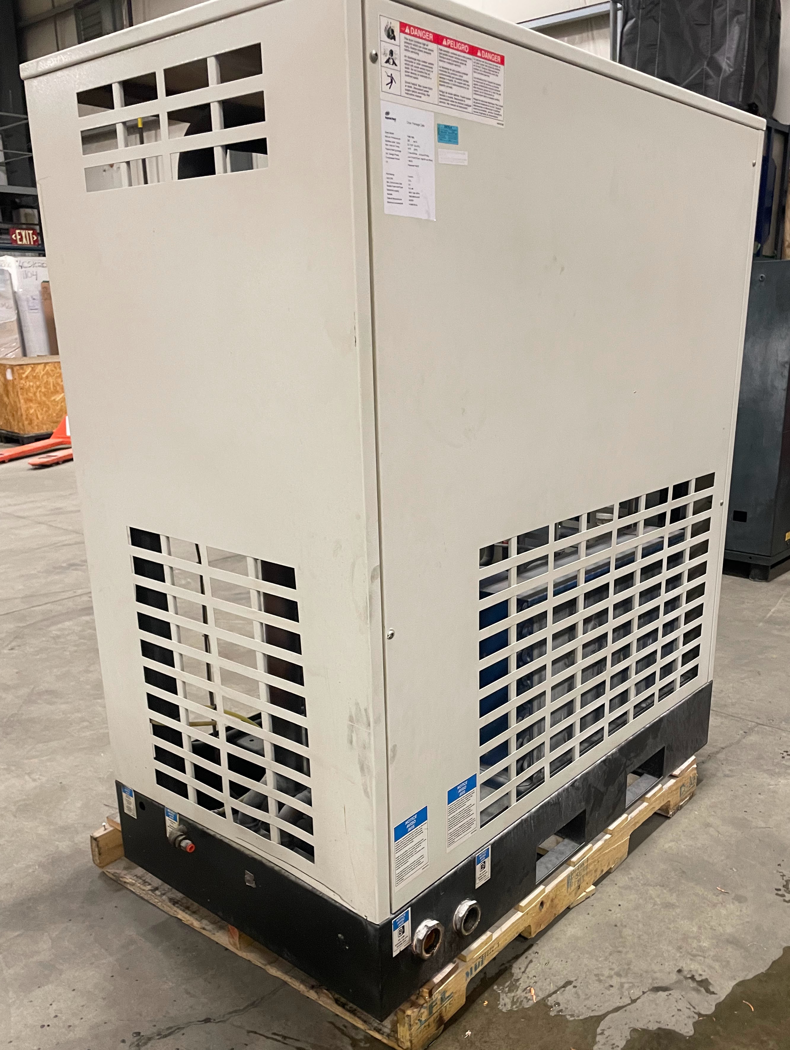 Large industrial HVAC unit with vented panels, installed on a wooden pallet inside a warehouse with concrete flooring.