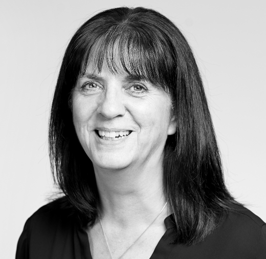 Black and white photo of a smiling person with shoulder-length dark hair and bangs, wearing a dark top.