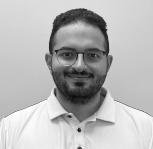 A person with glasses and a beard is wearing a white polo shirt, smiling at the camera against a plain background.