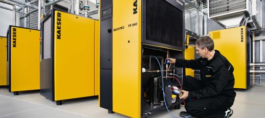 A technician performs maintenance on a yellow Kaeser industrial machine in a facility with additional similar machines visible in the background.