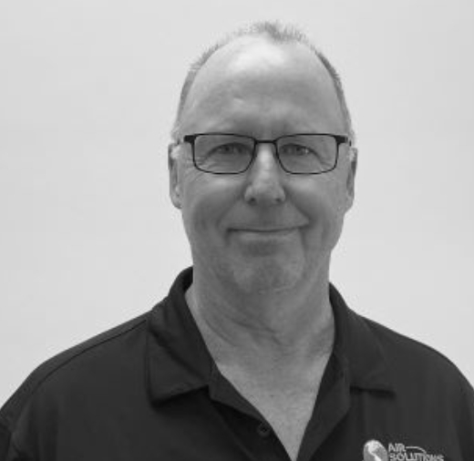 A man wearing glasses and a polo shirt with a logo on the right side, smiling at the camera against a plain background.