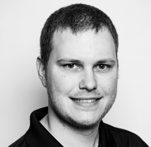 Black and white portrait of a smiling man with short hair, wearing a polo shirt, against a plain background.