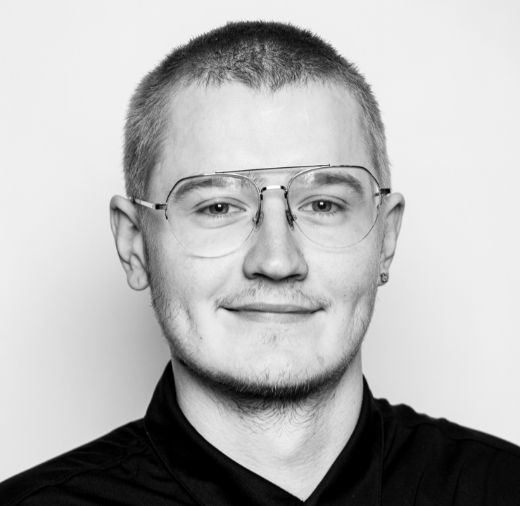 A person wearing glasses and a dark shirt is smiling slightly in this black and white portrait.