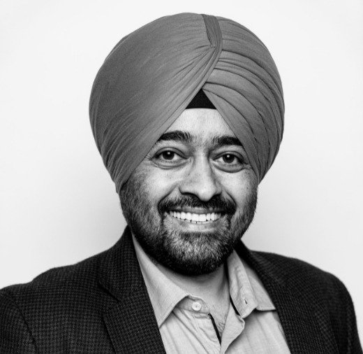 A person with a turban smiles while wearing a collared shirt and jacket in a black and white photo.