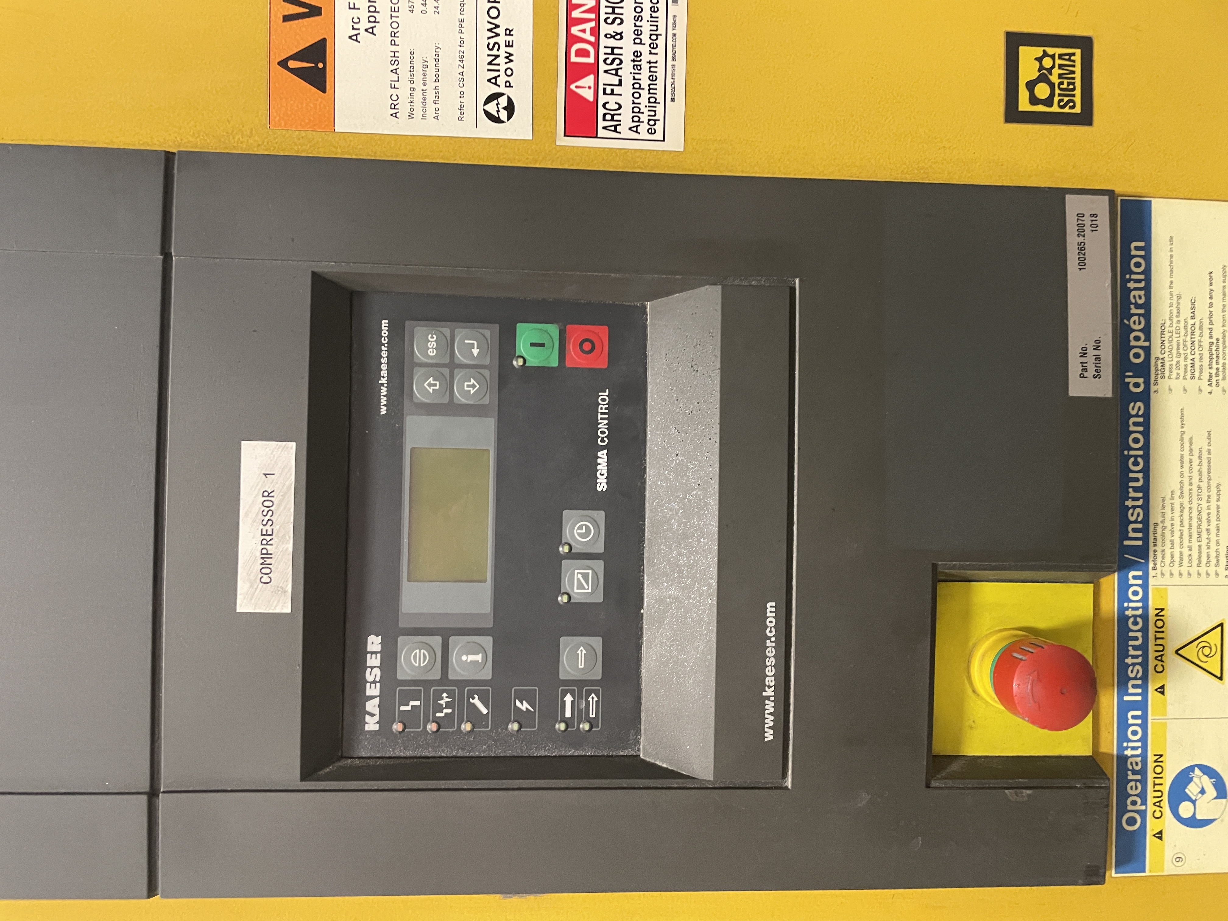 Control panel of a Kaeser compressor with digital display, buttons, emergency stop switch, and caution labels in English and French.