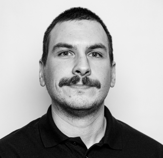 Black and white portrait of a man with a mustache, short hair, and a dark polo shirt, looking at the camera.