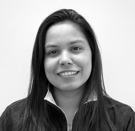 Black and white photo of a person with long hair wearing a jacket, smiling at the camera against a plain background.